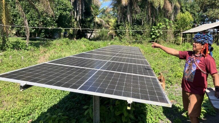 Ein Munduruku steht neben einem aufgebauten Solarpanel mit einer präsentierenden Geste