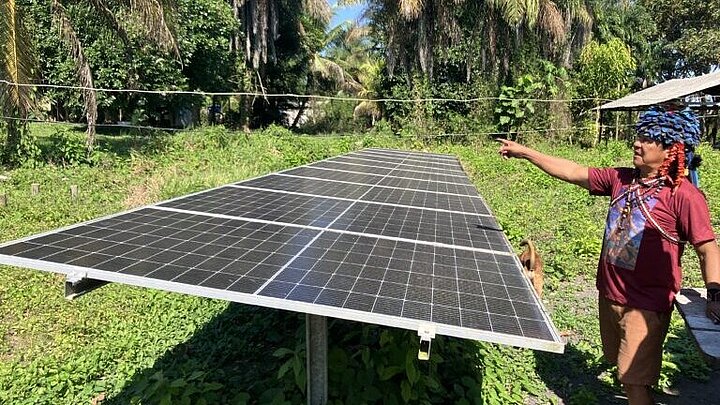 Ein Munduruku steht neben einem aufgebauten Solarpanel mit einer präsentierenden Geste