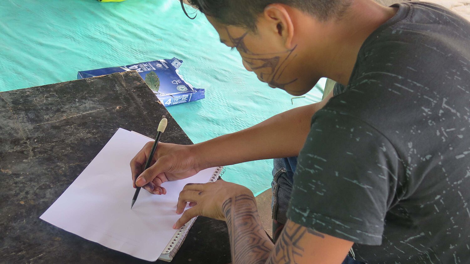 Ein indigener brasilianischer Junge sitzt am Tisch und schreibt