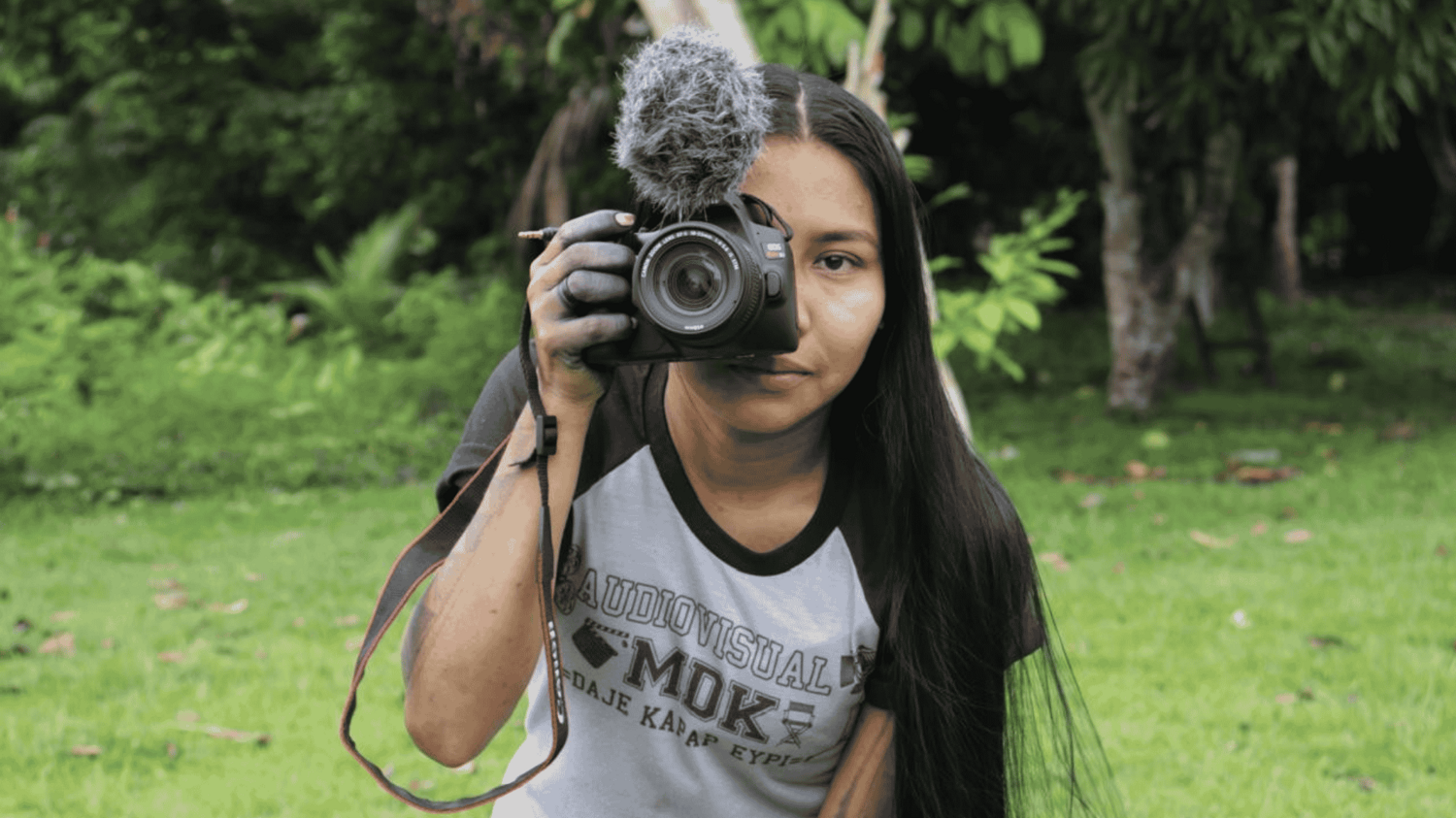 Eine Junge Frau mit Kamera in der Hand und einem T-Shirt mit dem Aufdruck Colectivo audiovisual