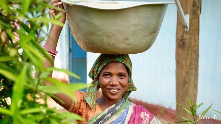 Eine indische Frau trägt eine Schüssel Wasser auf dem Kopf