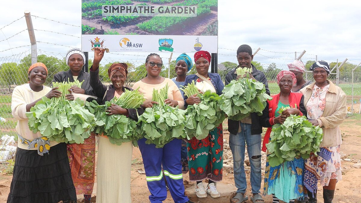 10 Frauen aus Simbabwe winken zufrieden mit Ernte in der Hand