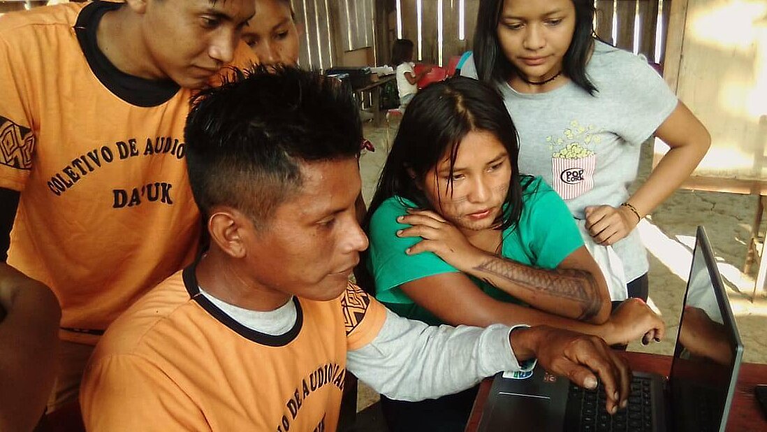 4 Jugendliche der Munduruku arbeiten mit einem Laptop. Sie tragen T-Shirts eines audiovisuellen Kollektivs