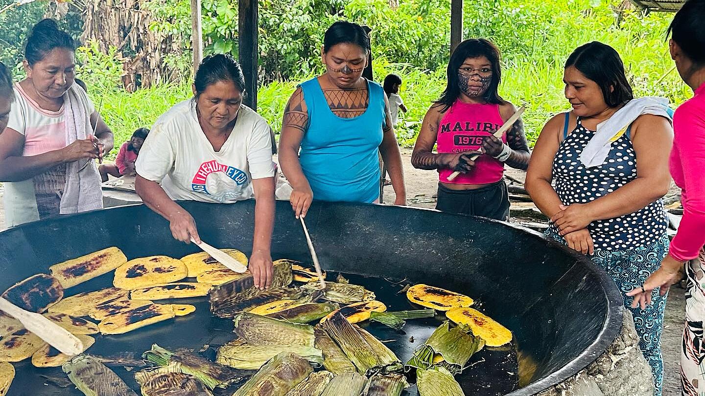 Eine Gruppe Munduruku steht um eine große Feuerstelle. Darauf wird Essen angebraten