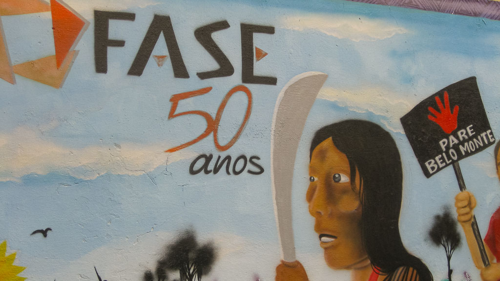 Wandgemälde_ FASE 50 Jahre, Person mit Machete und hinter ihr eine Person mit Schild " Stop Belo Monte"